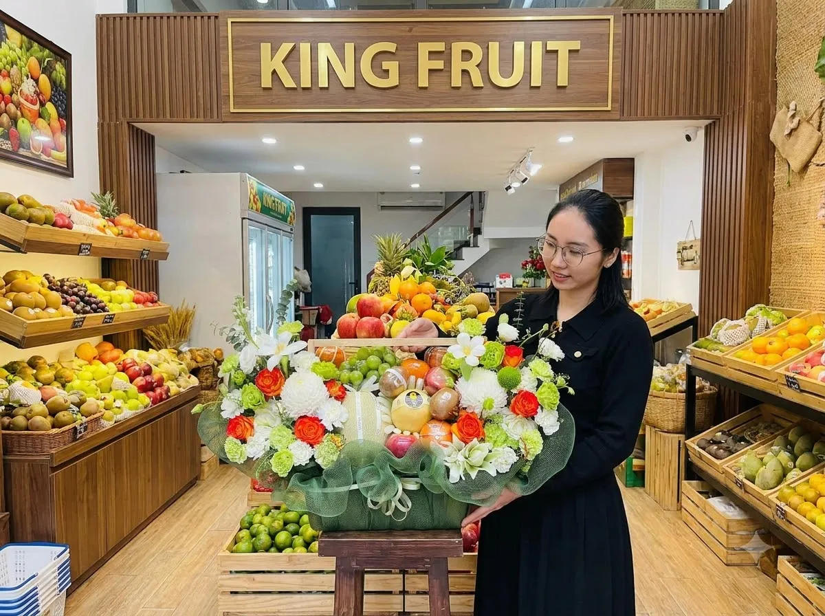 Nhân viên đặt giỏ hoa quả lớn kết hoa lên bàn dưới biển hiệu King Fruit trong cửa hàng. — King Fruit huyện Lạc Sơn, Hoà Bình