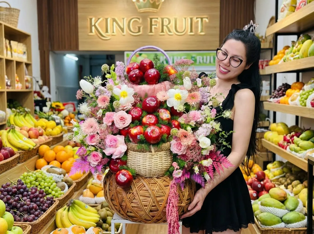 Nhân viên nữ đeo kính cười tươi ôm giỏ hoa quả có táo đỏ trong cửa hàng King Fruit. — King Fruit quận 10 HCM