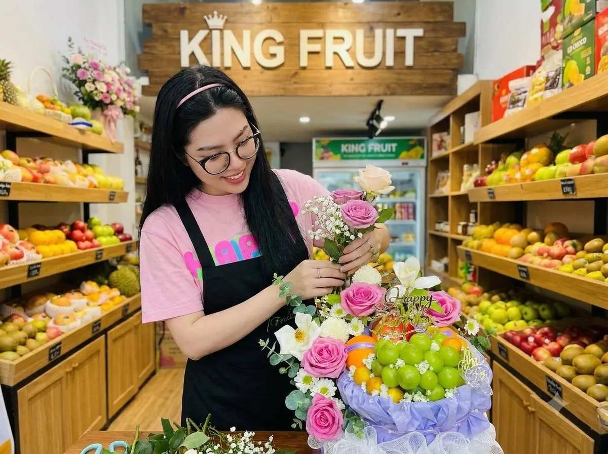 Nhân viên nữ đeo kính cắm hoa hồng vào giỏ hoa quả trong cửa hàng King Fruit. — King Fruit thị xã Ba Đồn, Quảng Bình