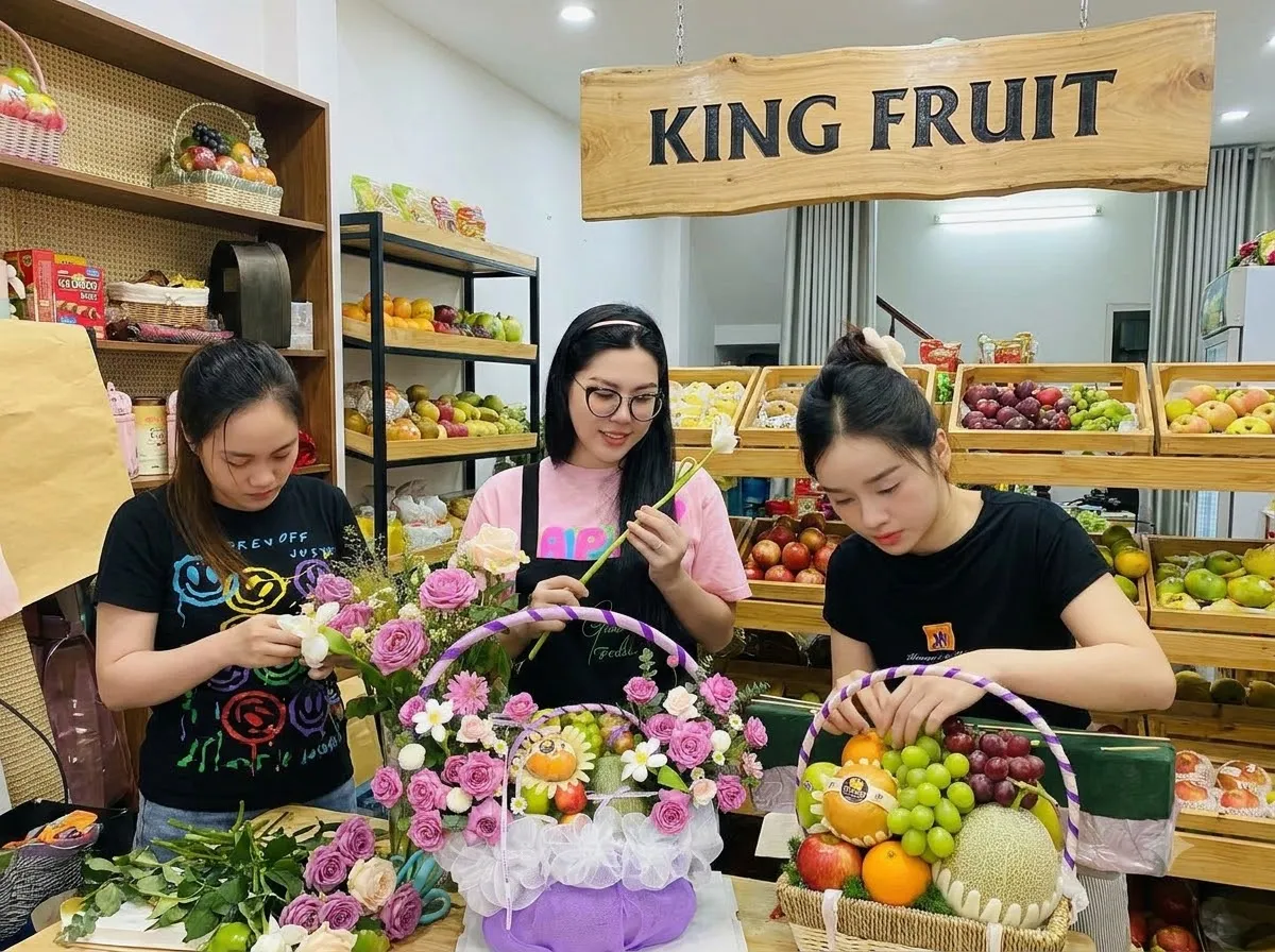 Ba nhân viên nữ kết hoa vào giỏ trái cây trên bàn trong cửa hàng King Fruit. — King Fruit Chư Prông, Gia Lai