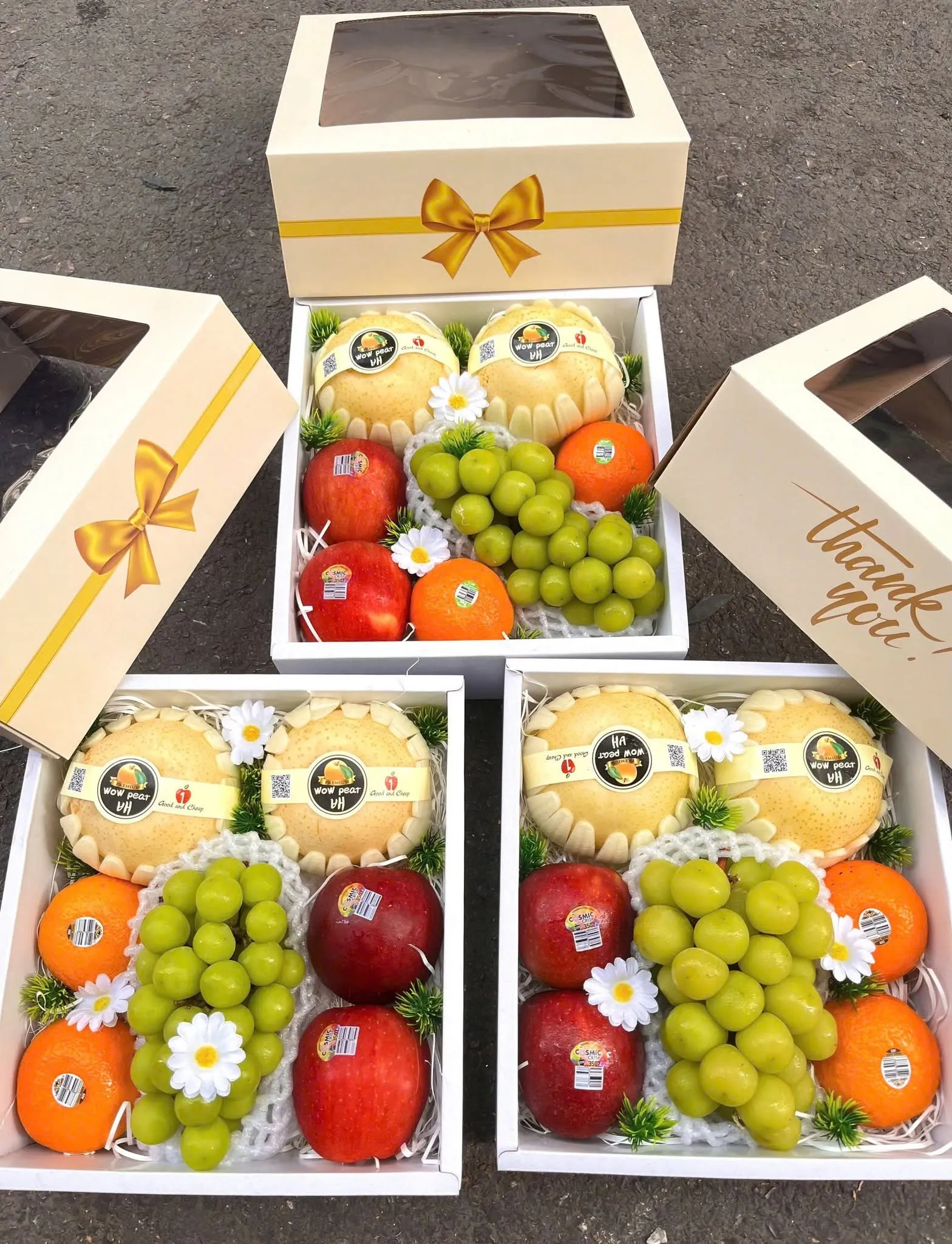 Ba hộp quà trái cây gồm dưa lưới, nho xanh, táo đỏ và cam xếp cạnh nhau trên nền đá. — King Fruit Quảng Ngãi