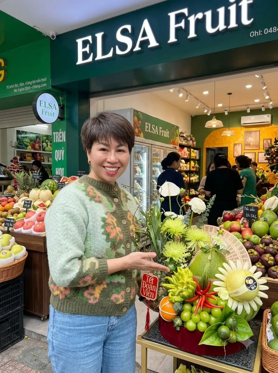 Nhân viên áo len xanh bên mâm quả cắm hoa cúc trước cửa hàng ELSA Fruit — ELSA Fruit huyện Nho Quan, Ninh Bình