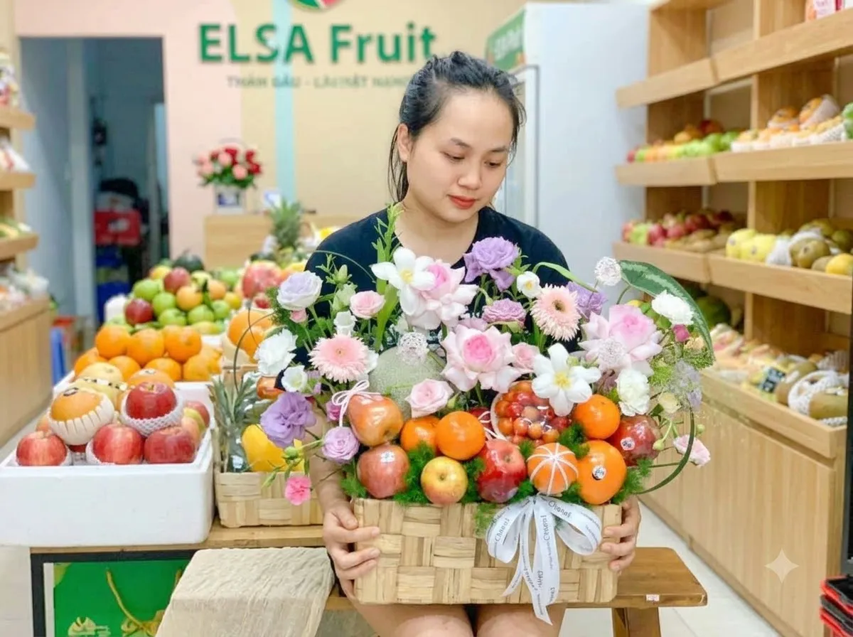 Nhân viên cầm giỏ mây táo, cam và hoa hồng, cúc trong cửa hàng ELSA Fruit — ELSA Fruit huyện Phú Riềng, Bình Phước