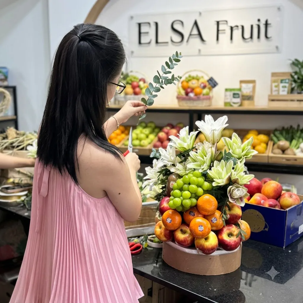 Nhân viên váy hồng cắm lẵng trái cây cam, táo, nho xanh và hoa ly trắng trong cửa hàng ELSA Fruit — ELSA Fruit Đức Hòa, Long An