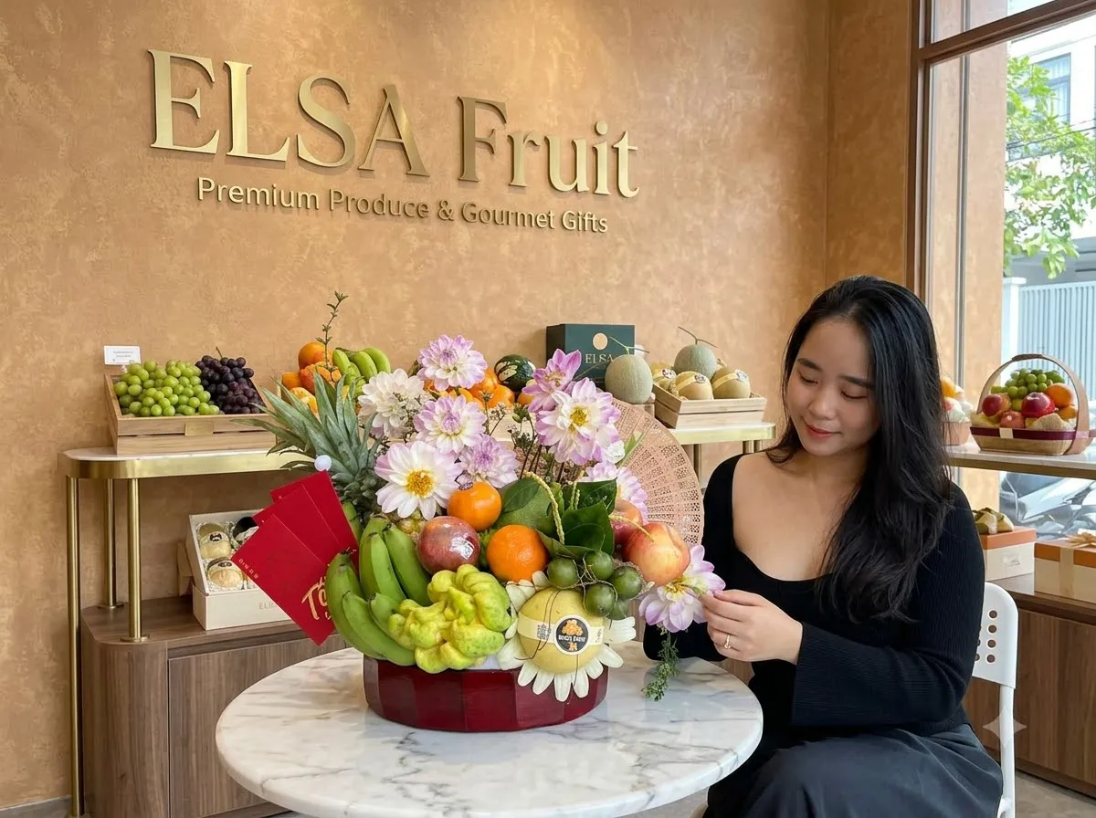 Khách ngồi bên mâm trái cây chuối, dứa và hoa nhiều màu trong cửa hàng ELSA Fruit — ELSA Fruit Thạnh Hóa, Long An