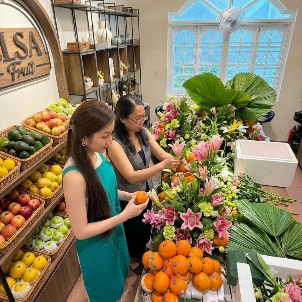 Hai nhân viên sắp xếp cam, xoài và hoa ly hồng trên quầy ELSA Fruit — ELSA Fruit huyện Trảng Bom, Đồng Nai