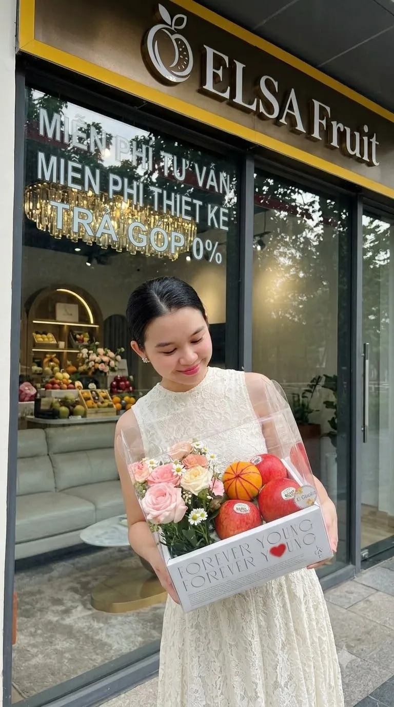 Nhân viên váy trắng cầm hộp quà trái cây và hoa hồng trước cửa ELSA Fruit — ELSA Fruit Tân Phước, Tiền Giang