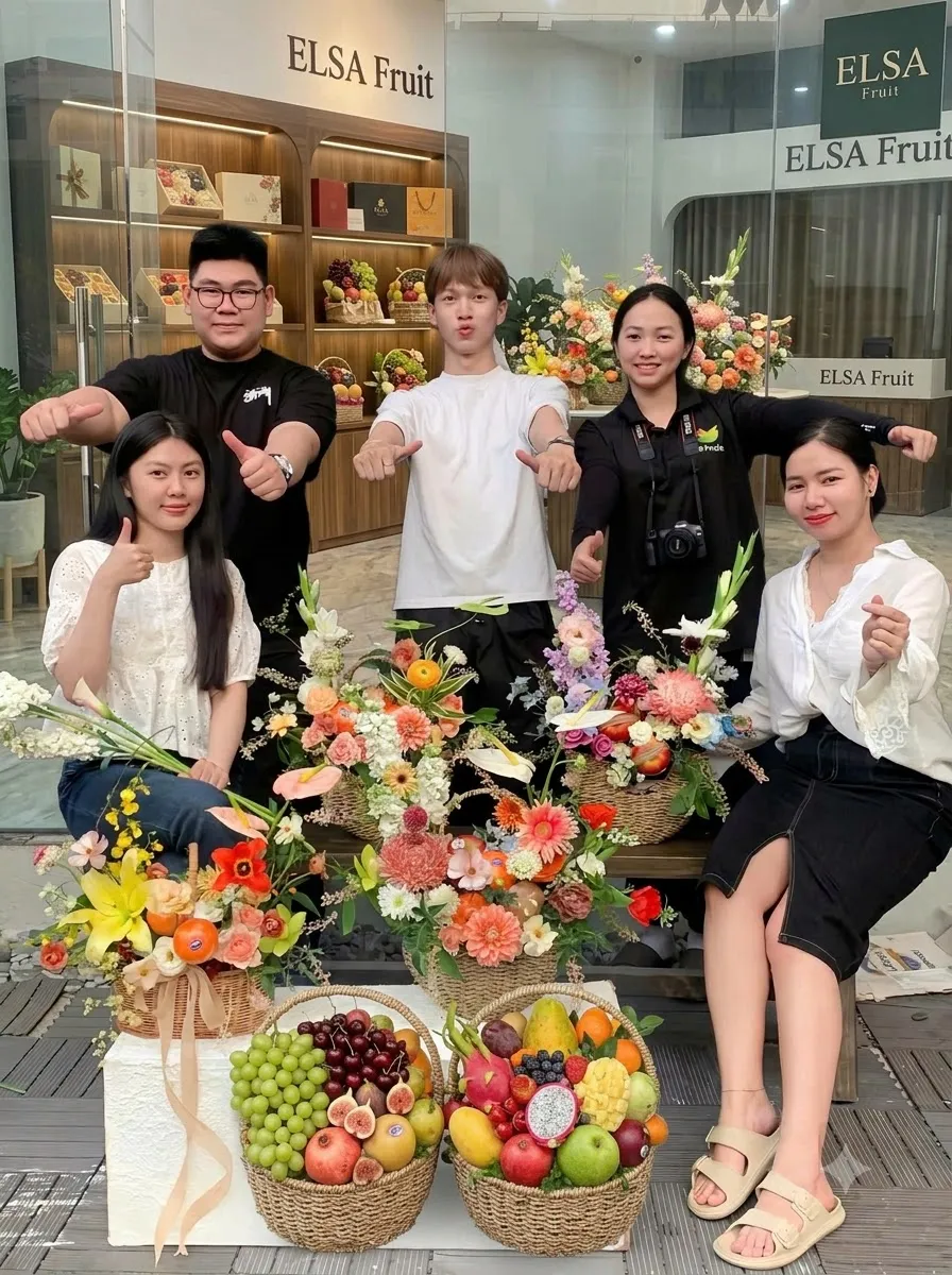 Nhóm nhân viên ELSA Fruit giơ ngón cái bên các giỏ hoa quả và hoa tươi trước cửa hàng — ELSA Fruit huyện Châu Thành, Kiên Giang