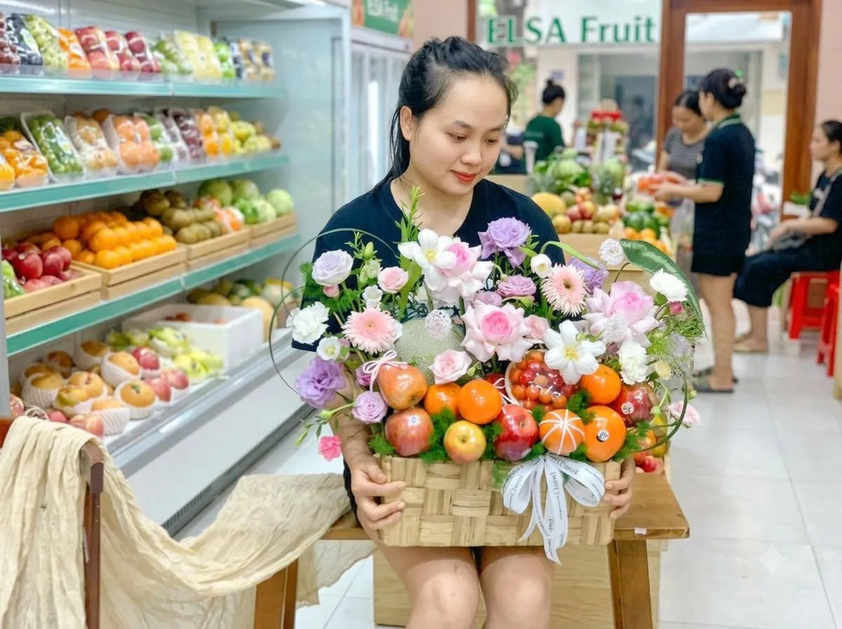 Nhân viên cầm giỏ mây cam, táo và hoa hồng, cúc trong cửa hàng ELSA Fruit — ELSA Fruit Đak Pơ, Gia Lai