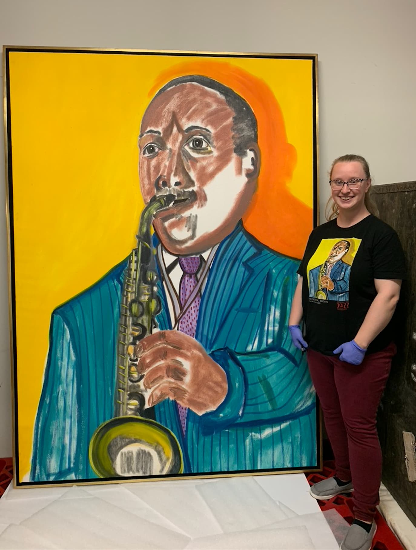 Curator Jordan M. standing beside a vibrant portrait of jazz legend Charlie Parker, featuring bold colors and expressive brushwork at the American Jazz Museum.