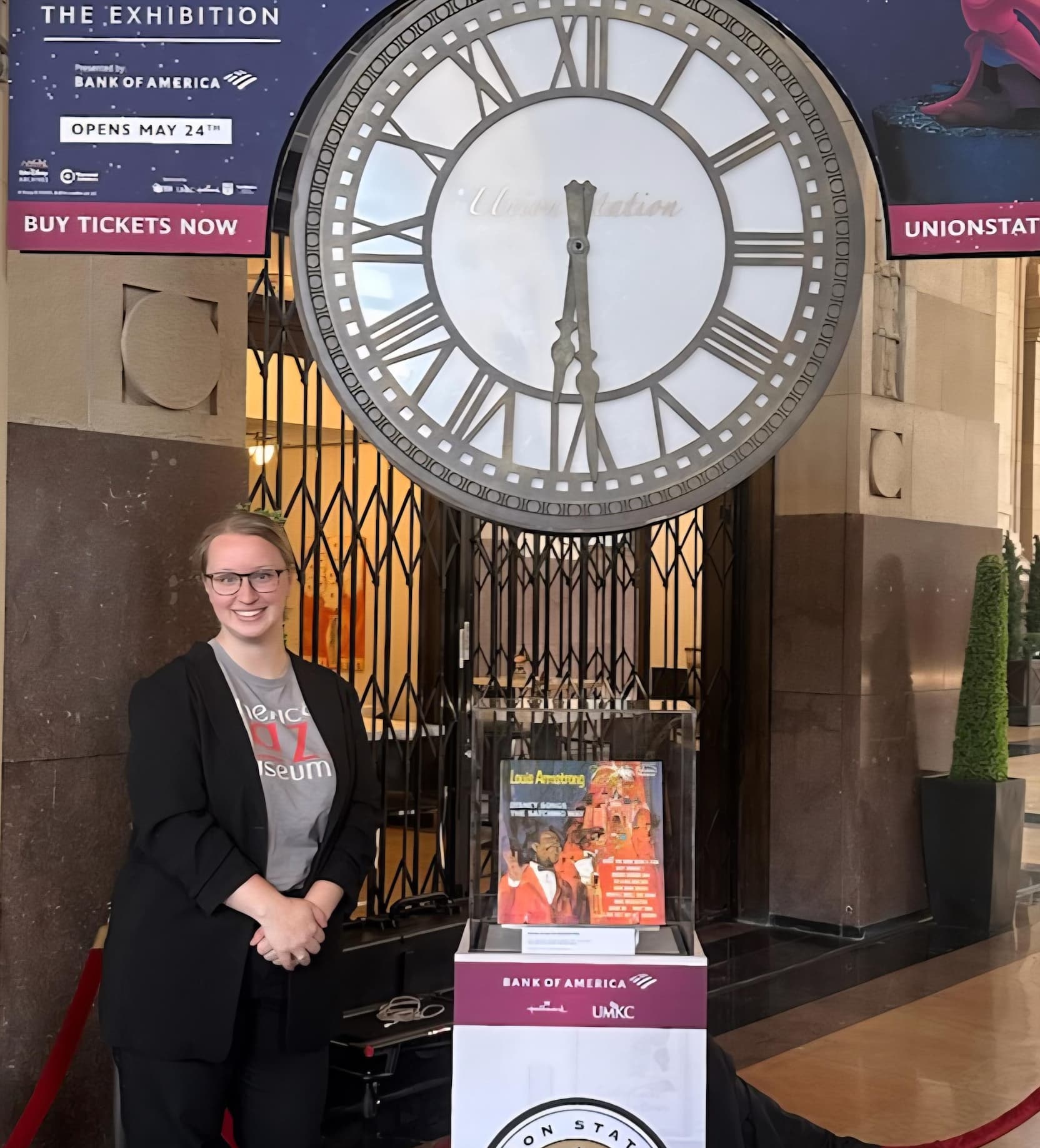 American Jazz Museum curator Jordan M. standing beside a Louis Armstrong album display at Kansas City’s Union Station under the historic clock.