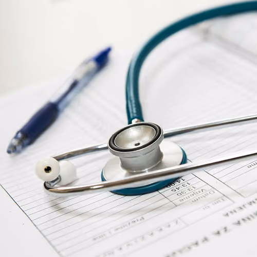 Stethoscope resting on a medical form with a blue pen in the background.
