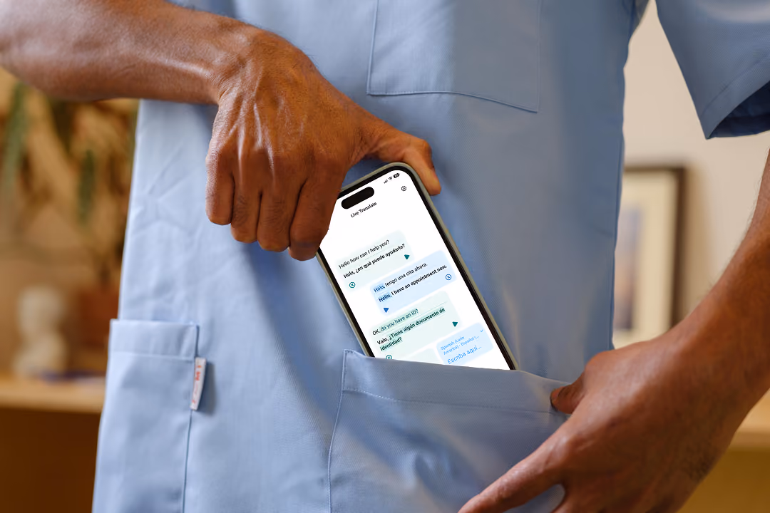 Healthcare staff in blue medical scrubs holding a smartphone displaying the multilingual medical translation app Care to Translate with conversation text in English and Spanish, partially inserting the phone into their scrub pocket.