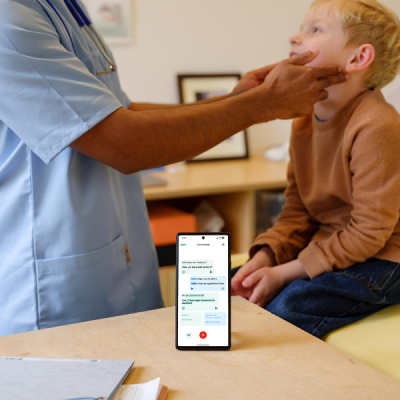 A male healthcare worker examining the throat of a young boy, a smartphone with the Care to Trnaslate translation app can be seen in the foreground