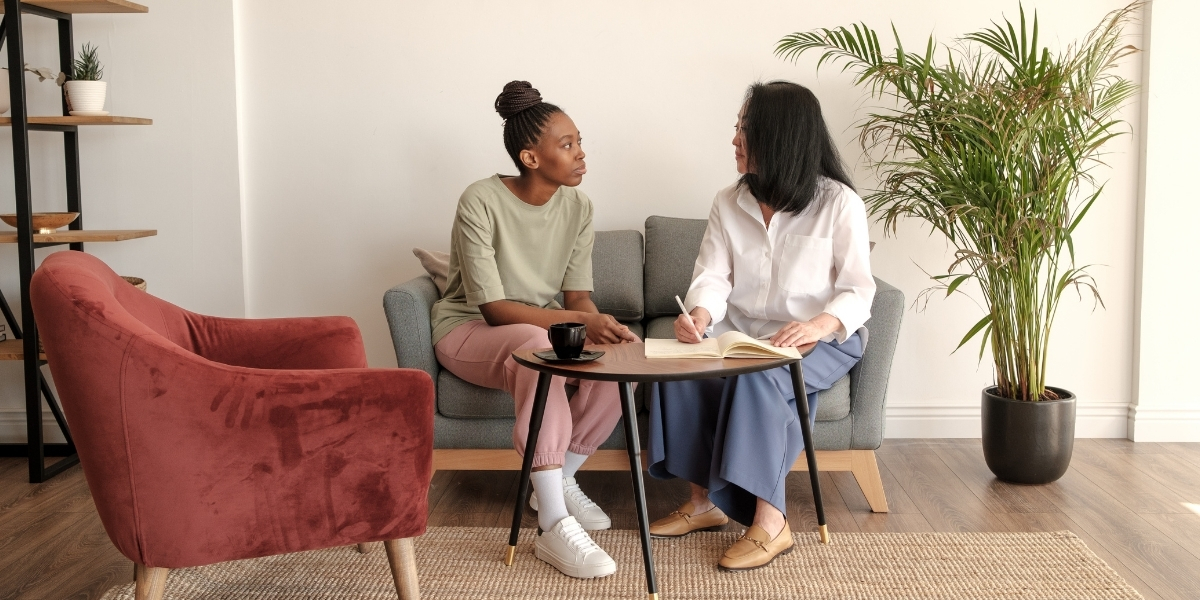 two females in a therapy session in a room with chair and a palm plant
