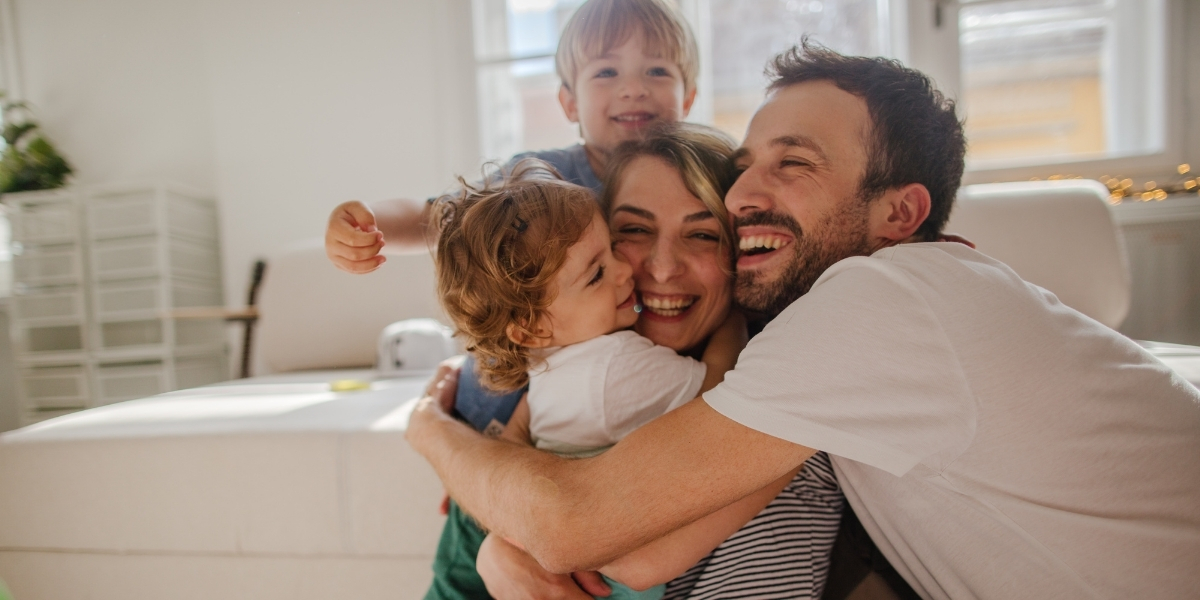 Family of four hugging and smiling in a living room