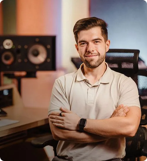 Tomasz Moskalski stojący przodem do kamery w studiu nagraniowym, z kontrolerem MIDI i interfejsem audio w tle – prowadzący kurs miksowania wokalu.