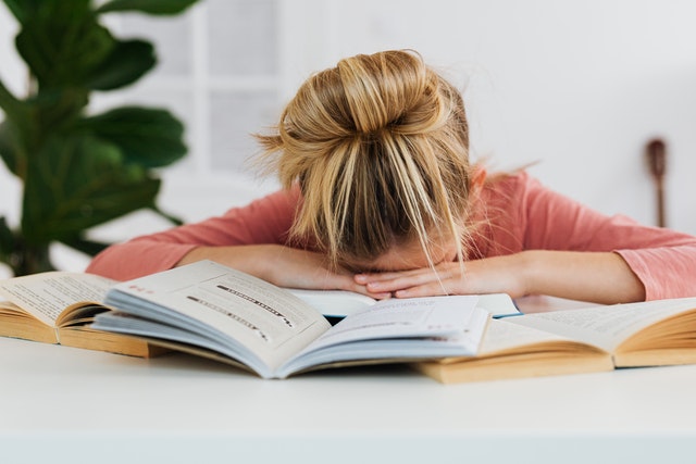 a girl with her head down on books while sitting at a desk.