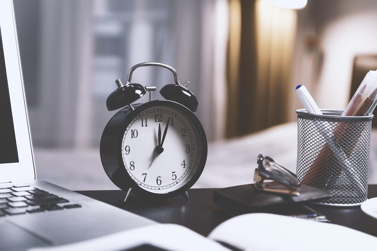 An alarm clock sitting on a desk next to a laptop.