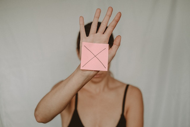 a woman with undiagnosed adhd holding a pink sticky note in front of her face with an x written on it