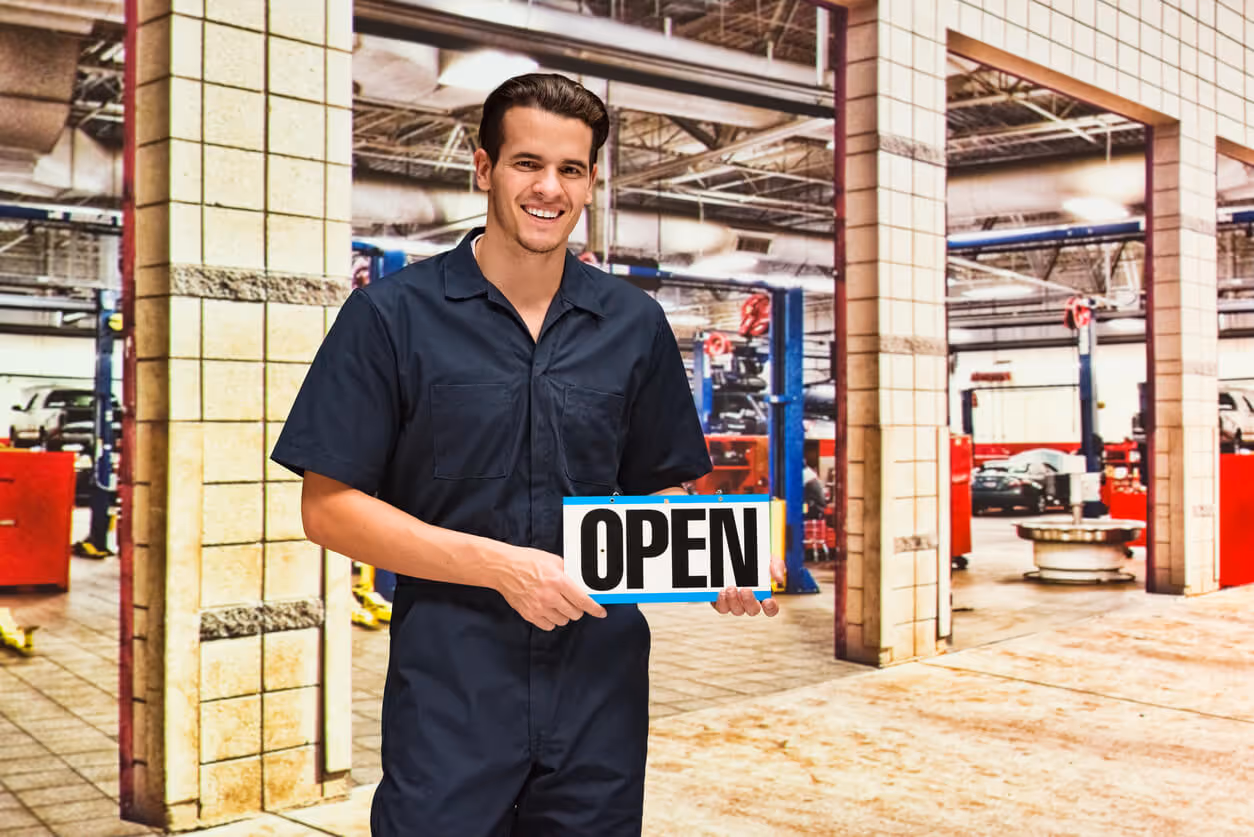NH Garage Keepers Insurance concept - Smiling mechanic holding open sign