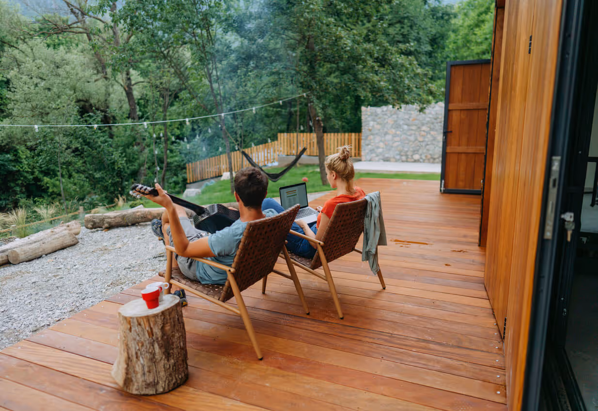 NH Airbnb Insurance concept - couple relaxing on deck while playing guitar and looking at laptop