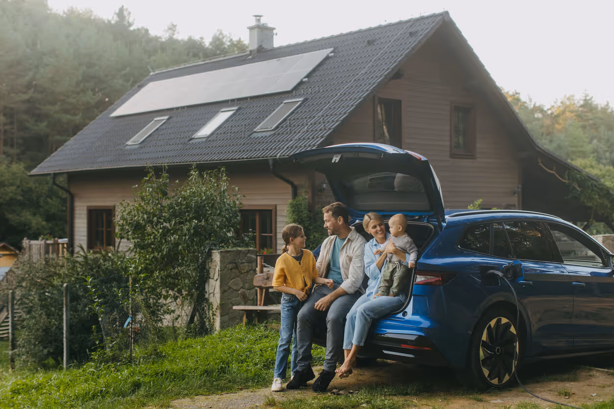 Family with electric car standing in front their house with solar panels on the roof.