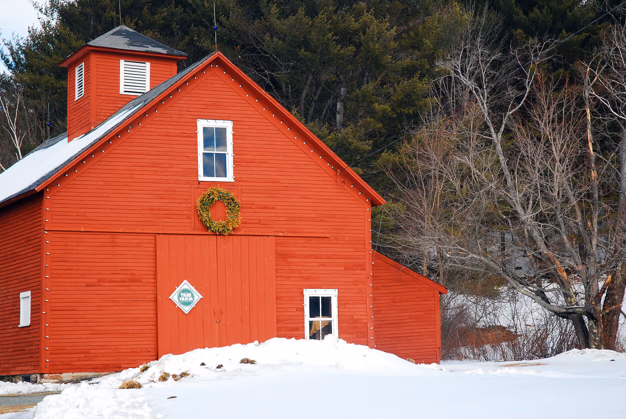 A red barn, surrounded by snow, is decorated for Christmas with a wreath