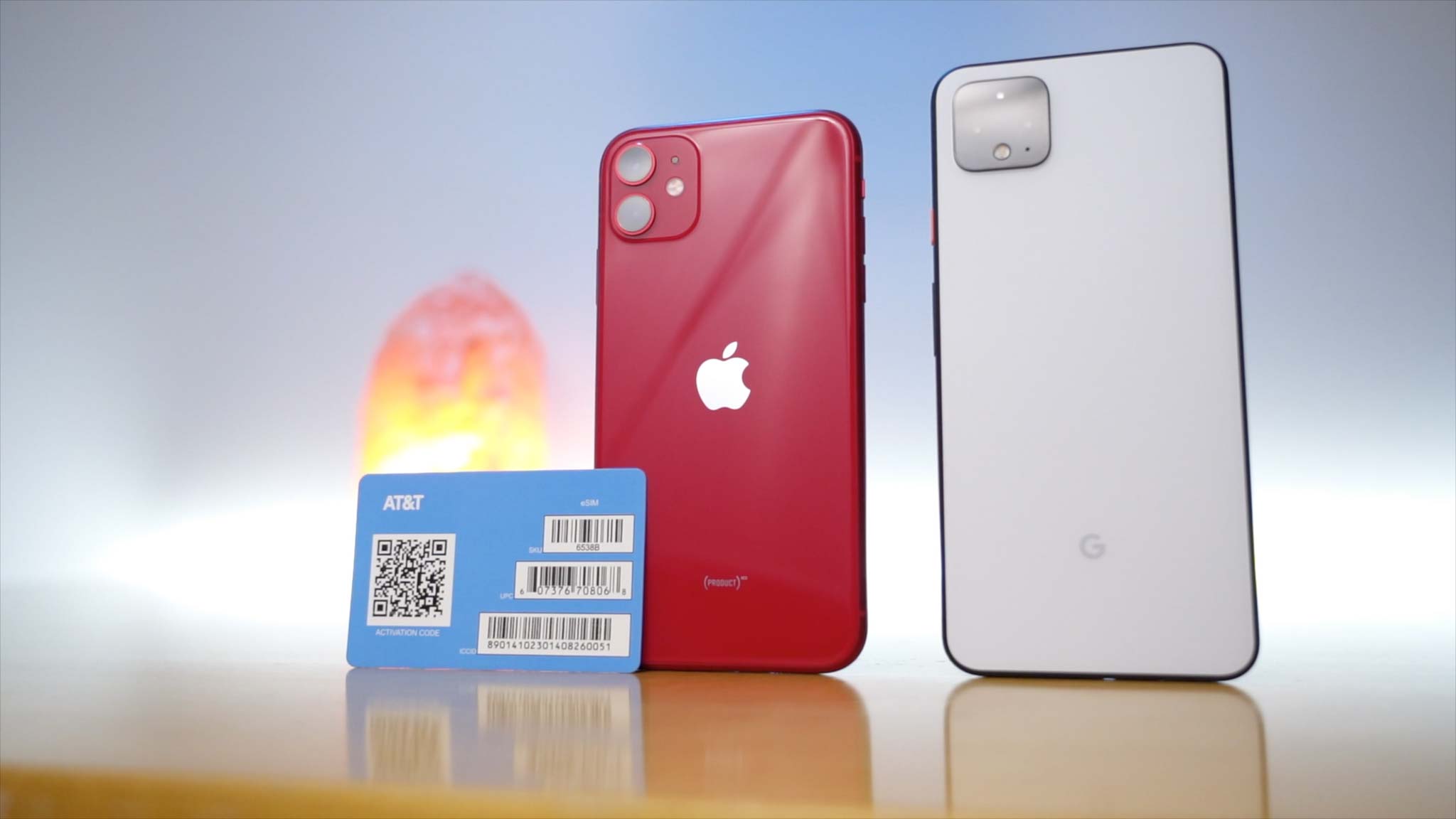 iPhone 11 in Product Red next to Clearly White Pixel 4 XL with AT&T eSIM card propped up on iPhone 11