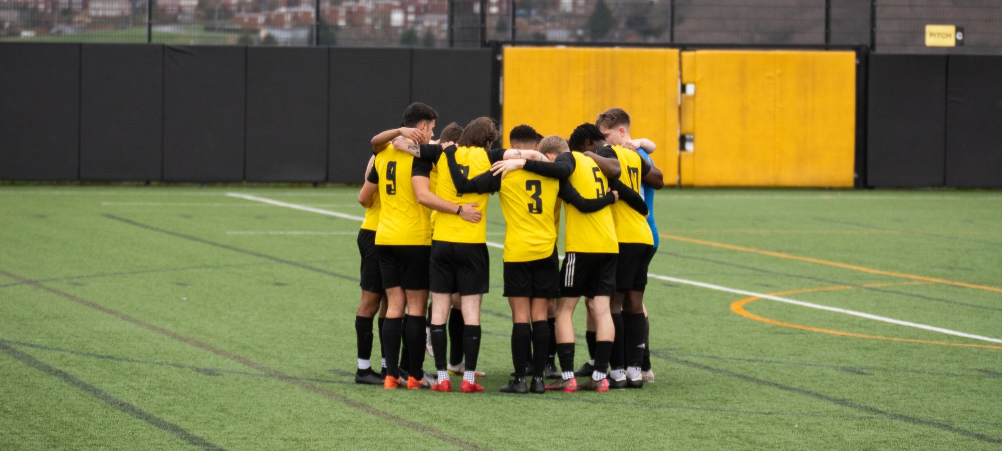 A sports team huddle on an astroturf pitch