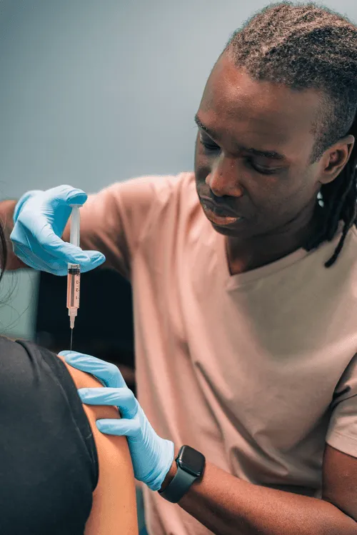 Dr Lewis wearing gloves administering an injection to a patient's upper arm.