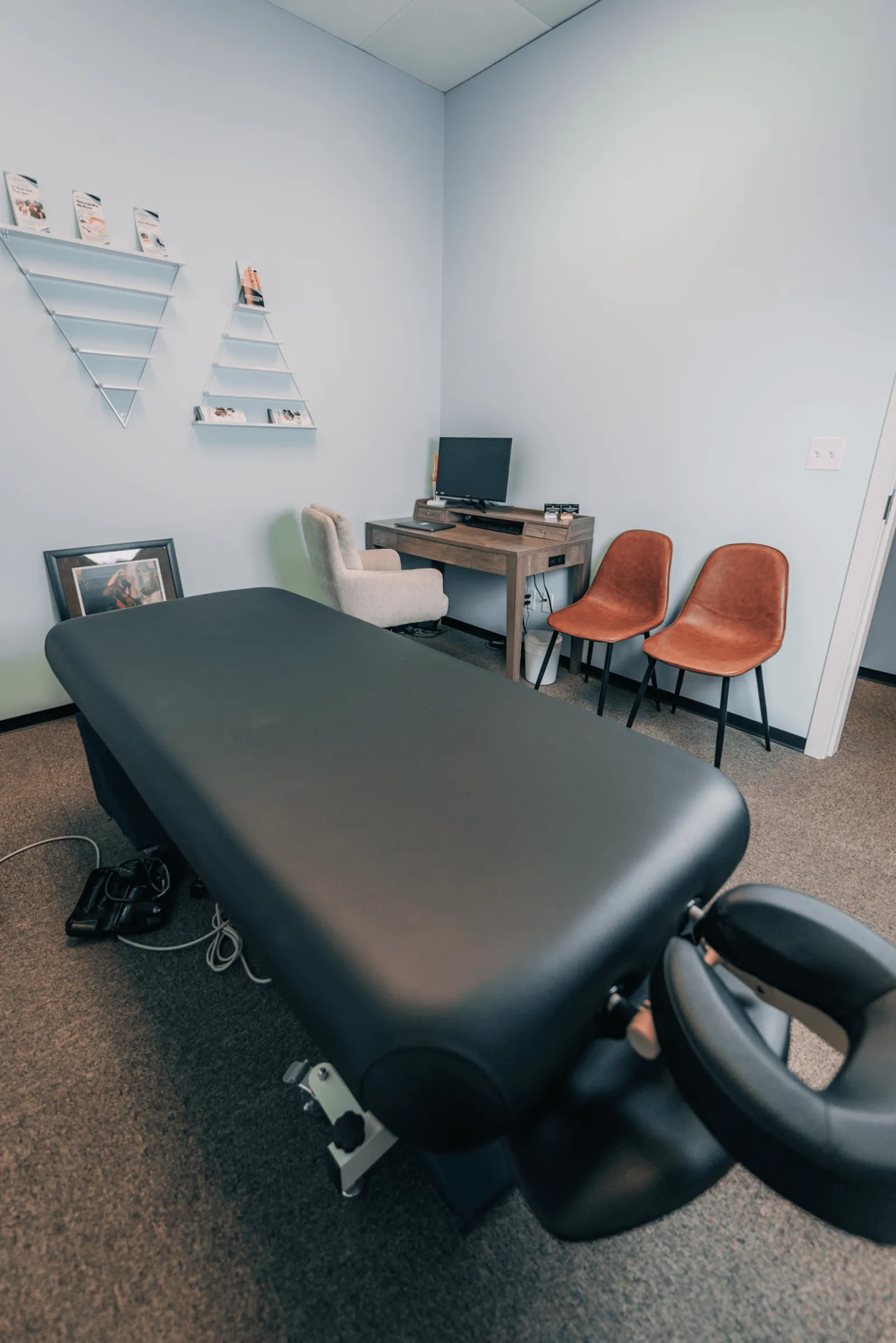 A well-organized massage therapy room with a treatment bed, chairs, and a desk.