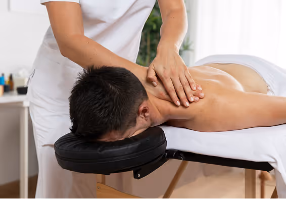 Massage therapist working on a client’s upper back on a treatment table.