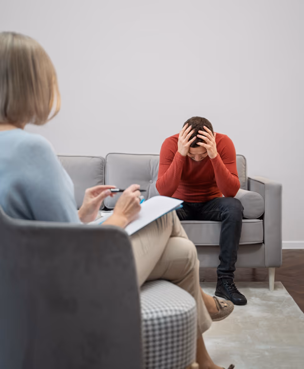 A man sitting on a couch with his head in his hands during a counseling session.