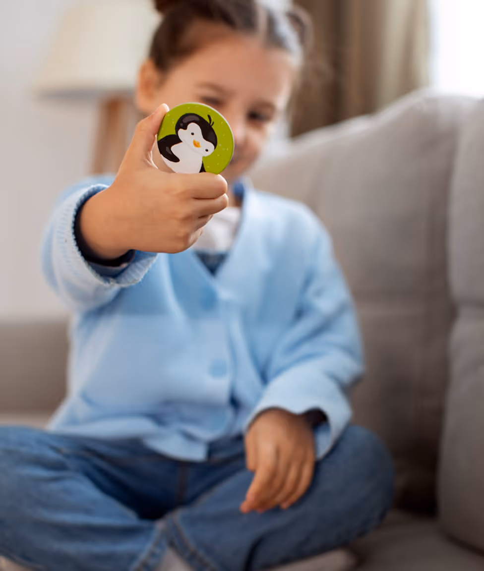 A child holding up a toy with a penguin illustration while sitting on a couch.