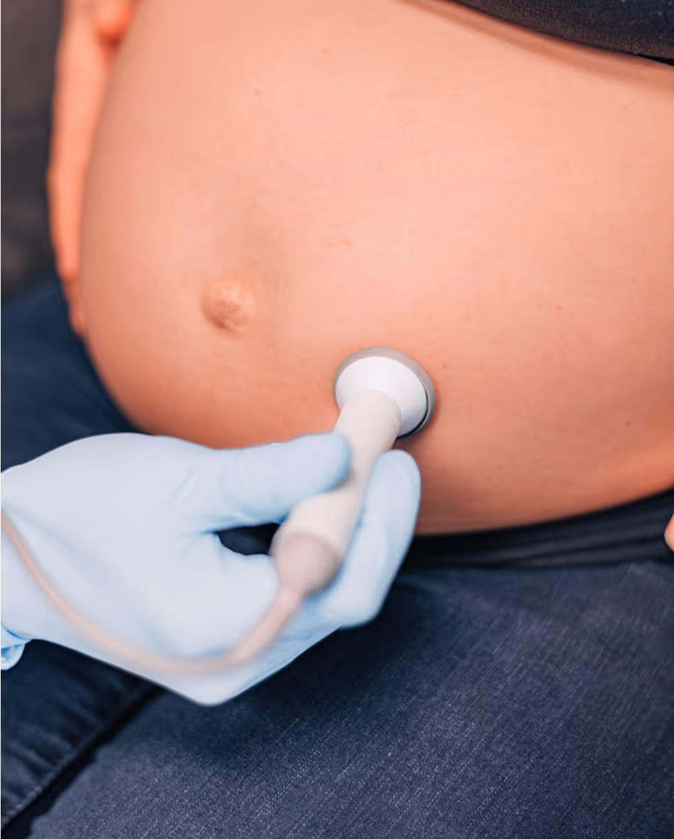 A woman is wearing a blue glove and holding a device to her belly.