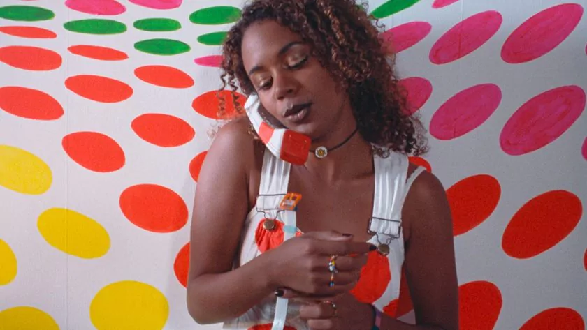 Movie still from Nowhere. A woman on a polka-dot phone in a polka-dot room, wearing polka-dot overalls.
