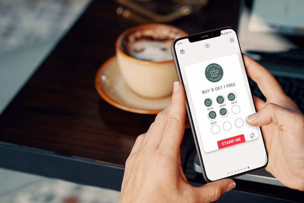 Hands holding phone with digital loyalty card over a coffee