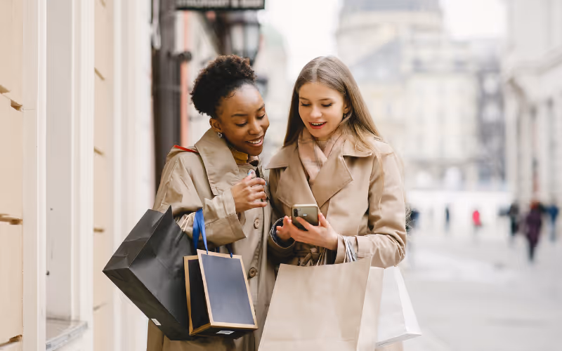 Two young women looking at the phone and holding shopping bags