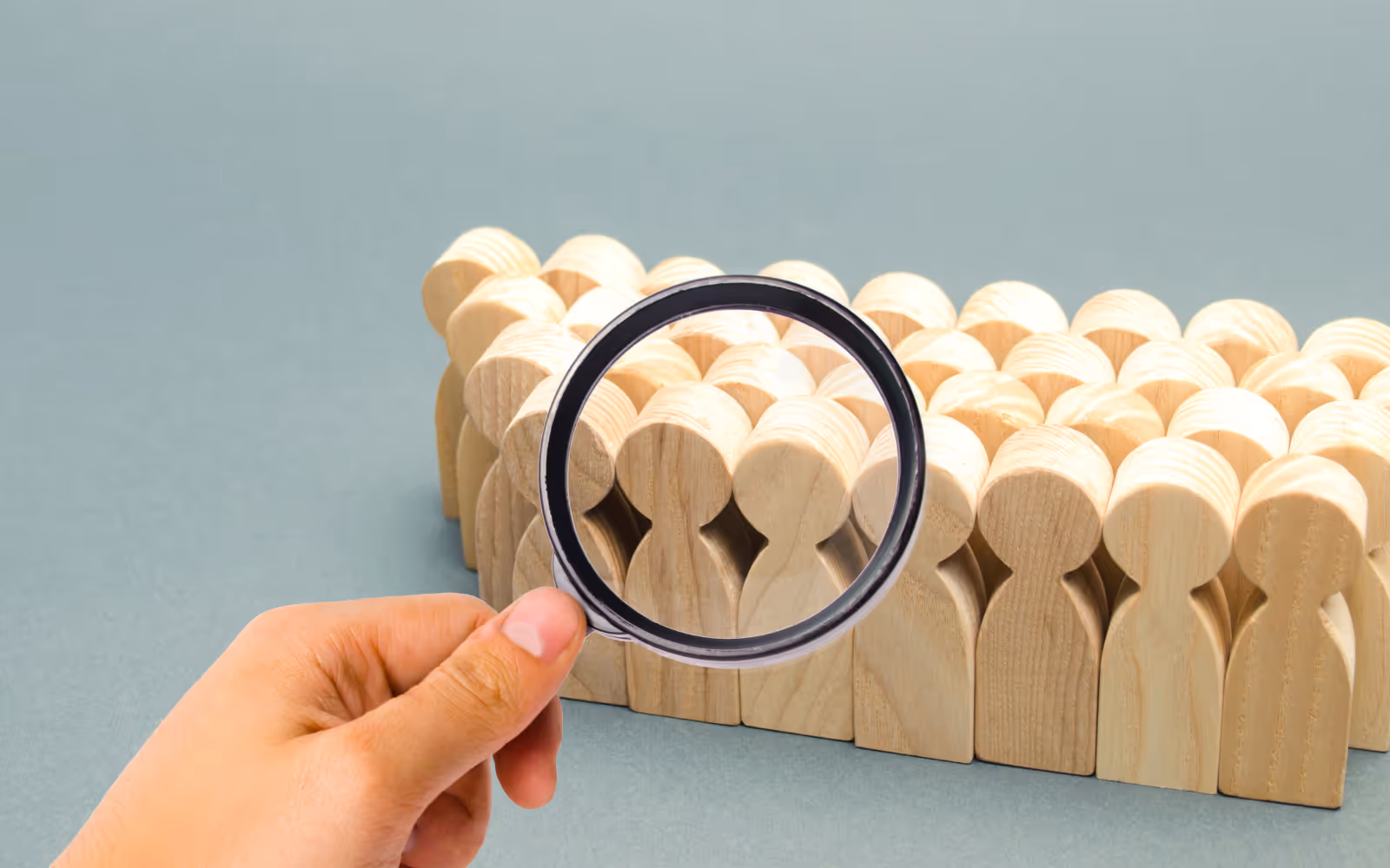 A magnifying glass looks over a group of wooden blocks which represent people, focusing on a select few. 