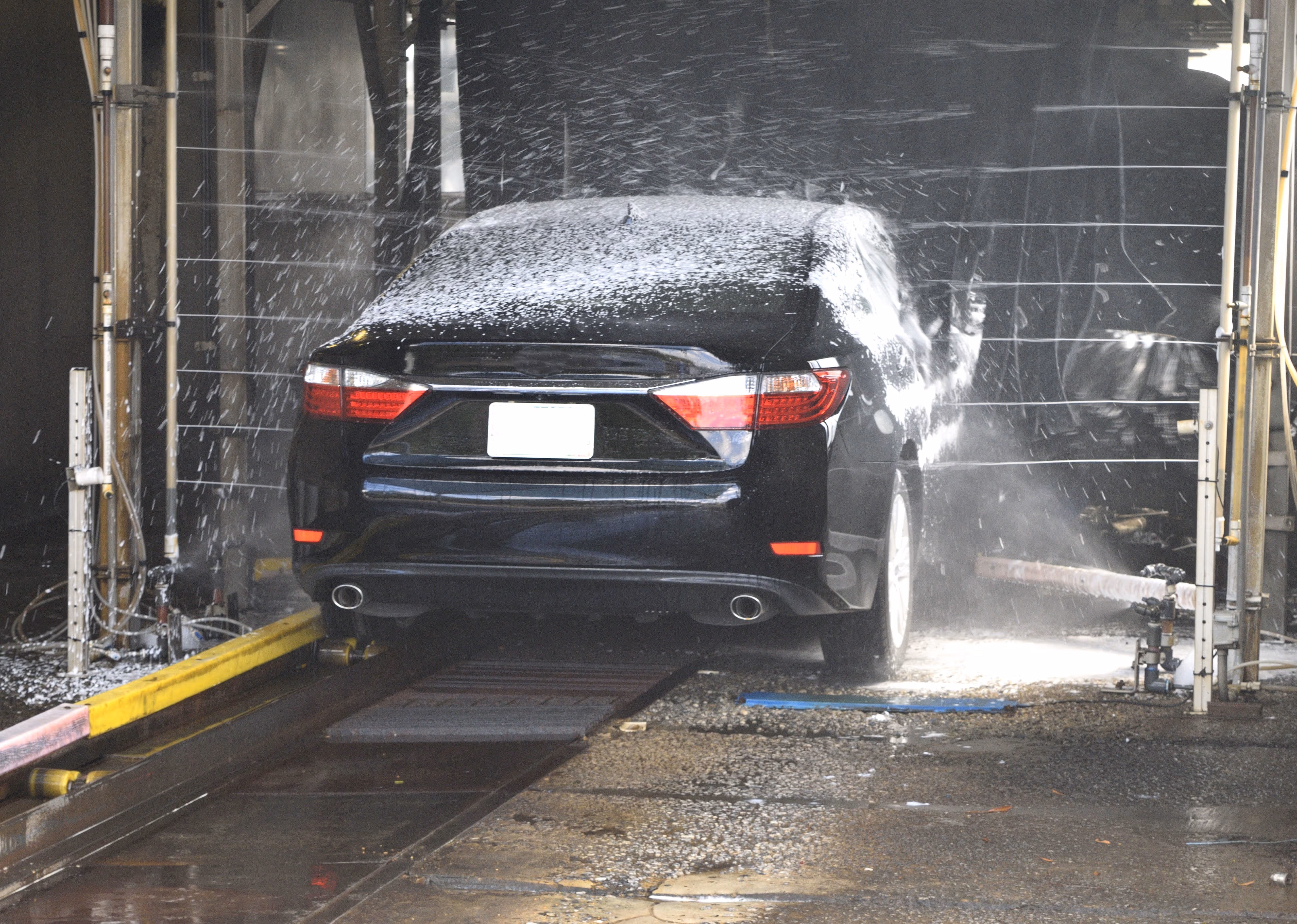 Car being sprayed with water in a professional car wash, highlighting the cleaning and detailing process.