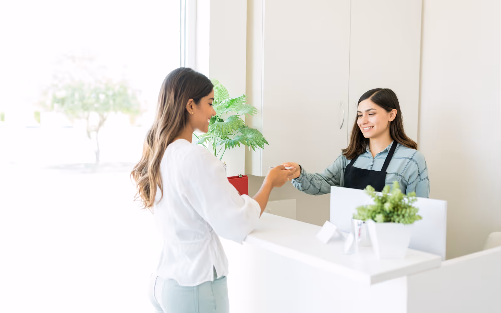 Woman handing a card to a customer at a reception desk.