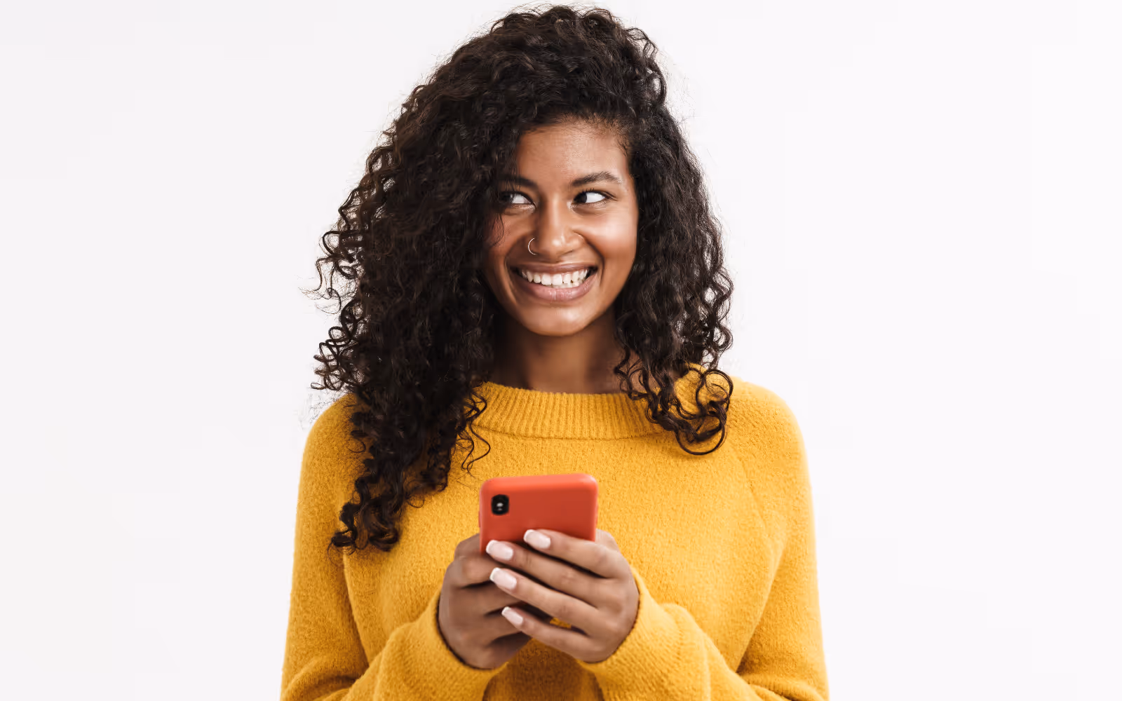 Woman in front of white background smiling whilst holding a mobile phone.