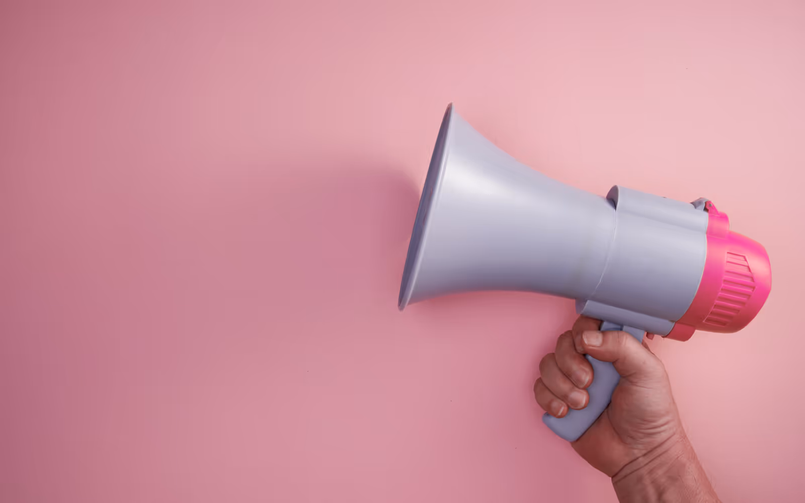 A megaphone in someone's hand against a pink backdrop. 