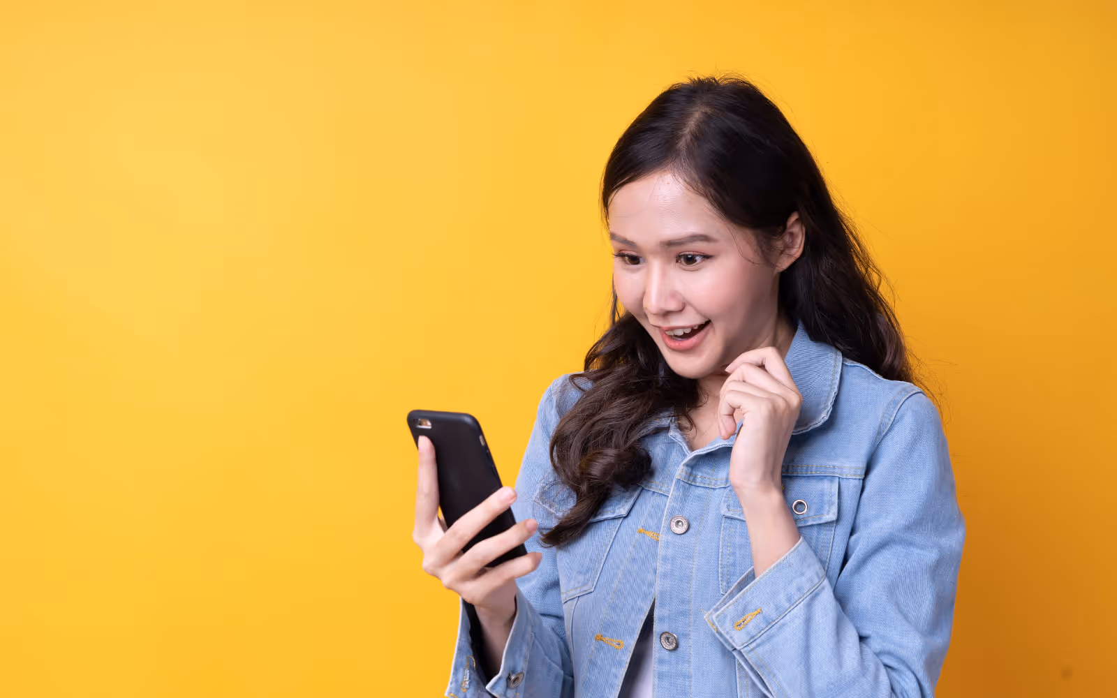 A woman looking at their phone smiling in front of a yellow background. 