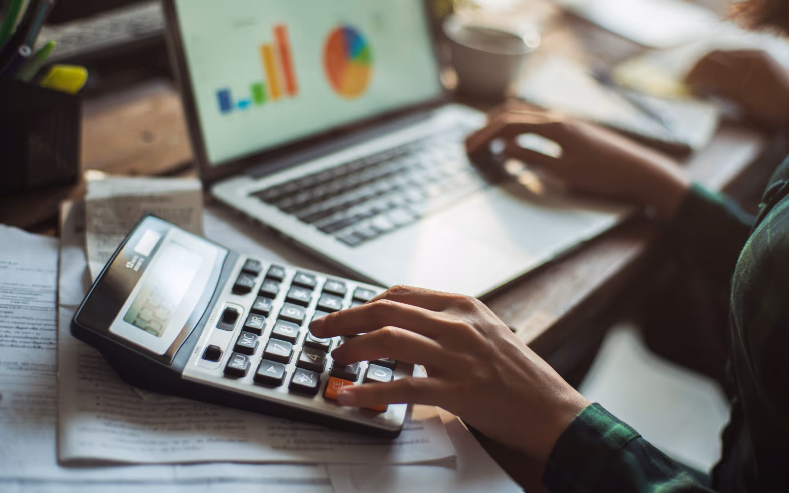 Person typing on a laptop with a calculator next to it