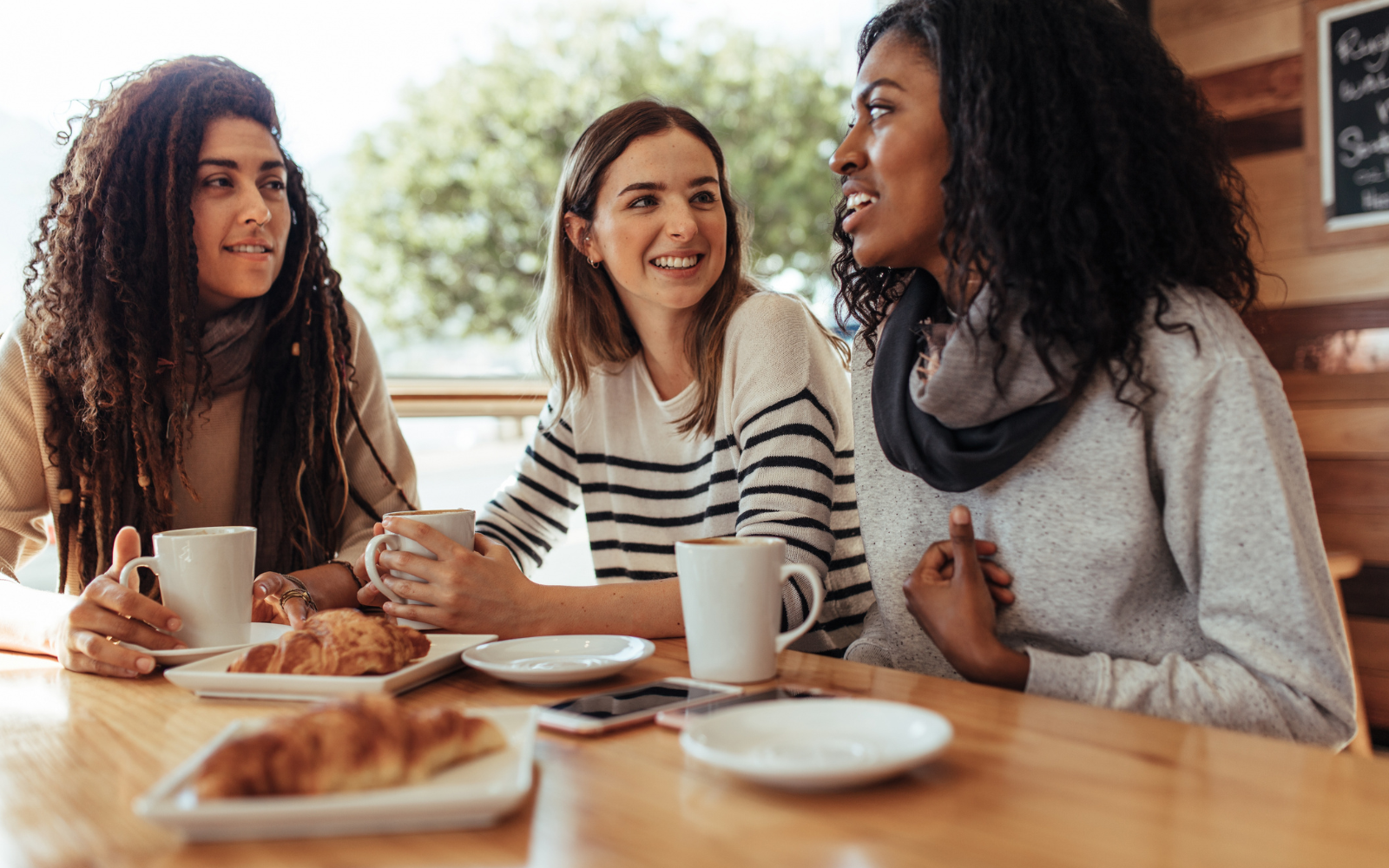 Coffee shop customer sharing digital loyalty program rewards with a friend, driving referrals
