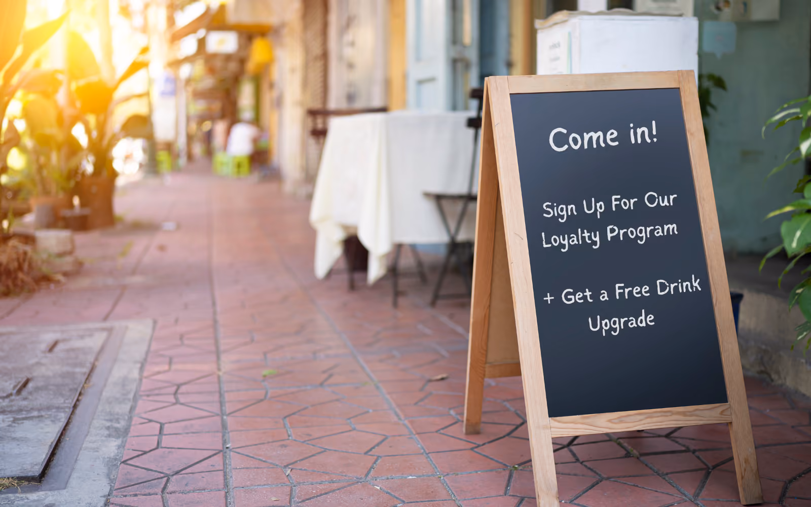 Small business owner behind a cafe counter promoting a loyalty program with a sign and counter card display at point of sale.