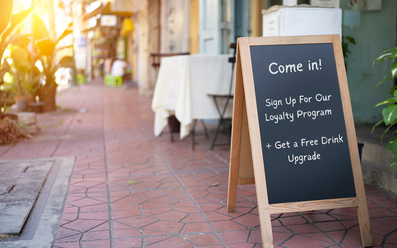 Small business owner behind a cafe counter promoting a loyalty program with a sign and counter card display at point of sale.