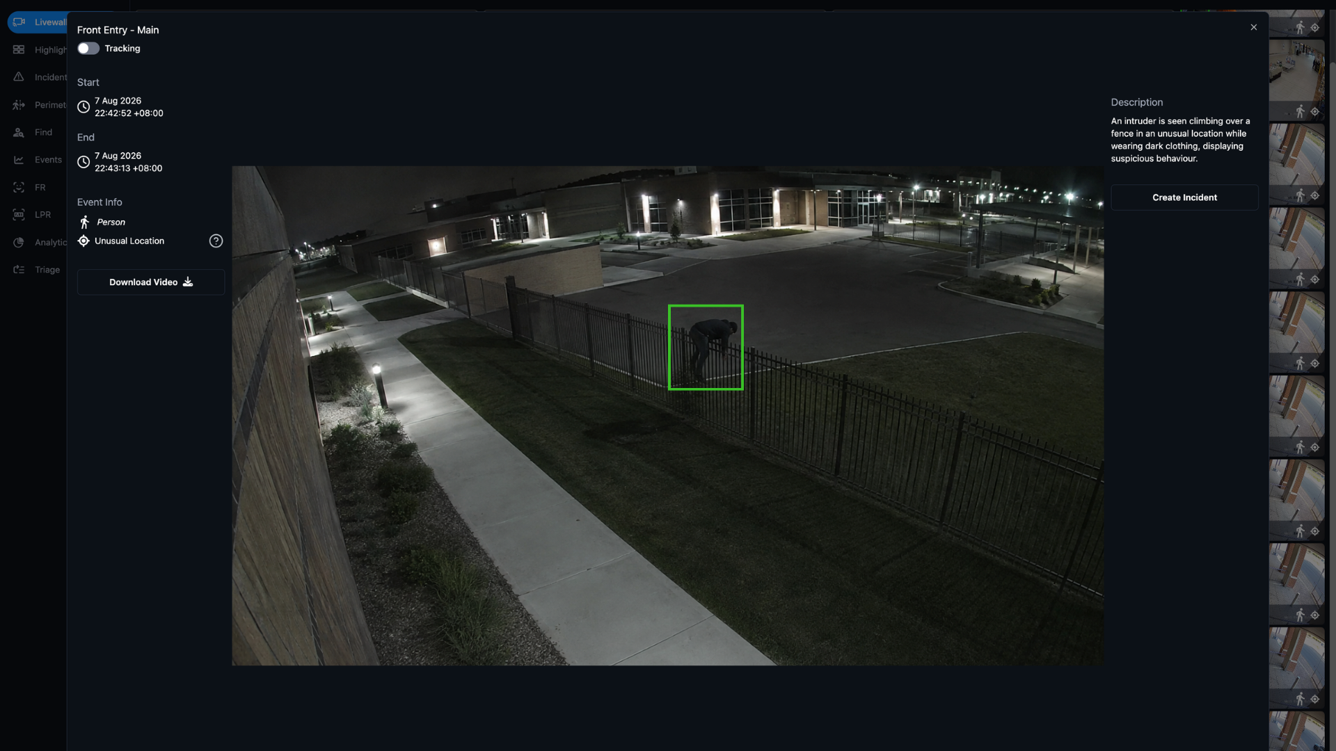 Person dressed in dark clothing climbing over a metal fence at night in a fenced area outside a building.
